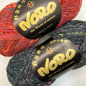 May include: Two skeins of Noro yarn, one red and one dark blue with multi-colored flecks. The yarn labels are black with gold lettering and say "Noro, the World of Nature, Made in Japan".