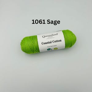K&ouml;nnte beinhalten: Eine Garnrolle in Gr&uuml;n mit der Aufschrift "Queensland Collection Coastal Cotton Pure Soft Cotton" und dem Farbcode 1061 Sage.