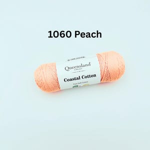 K&ouml;nnte beinhalten: Ein Kn&auml;uel peachfarbenes Garn mit der Aufschrift "Queensland Collection Coastal Cotton Pure Soft Cotton" und dem Farbcode 1060 Peach.