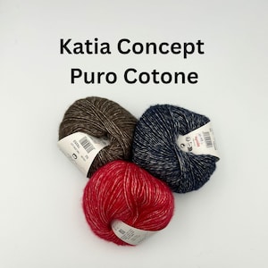 May include: Three skeins of Katia Concept Puro Cotone yarn in brown, navy blue, and red. Each skein has a white label with text and a barcode. The yarn is tightly wound and appears soft, ideal for knitting or crochet projects.