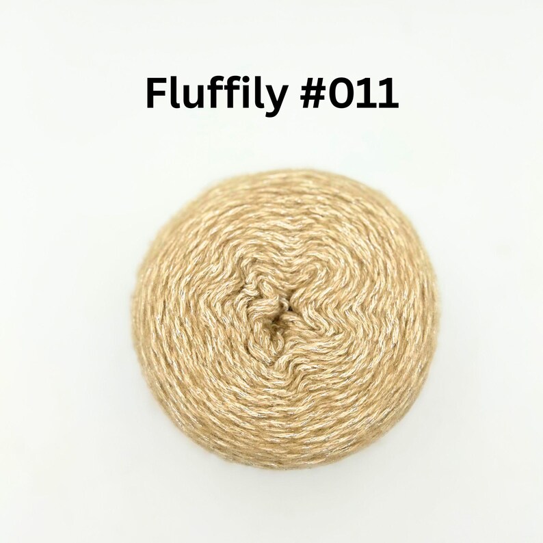 May include: A ball of light tan yarn with the text "Fluffily #011" in black. The yarn has a textured, swirled appearance, and is set against a white background. Suitable for knitting and crochet projects.