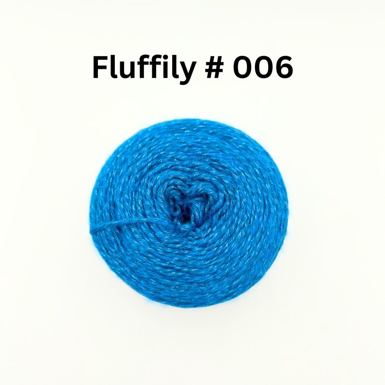 May include: A vibrant blue ball of yarn, labelled "Fluffily # 006", sits against a white backdrop. The yarn is tightly wound, showing texture, with a single strand extending from the ball. Suitable for knitting and crochet.
