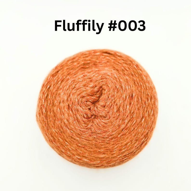 May include: A ball of orange yarn with the text "Fluffily #003" in black. The yarn has a warm, earthy tone and a slightly textured appearance. The yarn is tightly wound, forming a compact sphere.