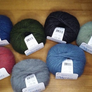 May include: Seven balls of yarn in various colors, including blue, green, gray, and red. Each ball has a label that says "Vento" and "Bricoo".
