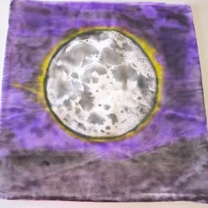 May include: A square, tie-dye fabric with a full moon design. The moon is white and gray with a yellow halo, set against a purple and gray background. The fabric has a soft, textured appearance.