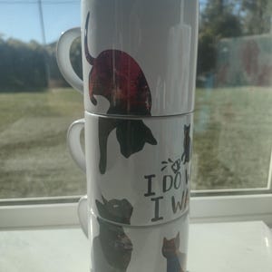 May include: Three white ceramic mugs stacked, each with a different cat design. The mugs feature various cat illustrations in black, brown, and orange, with the text "I DO WHAT I WANT".