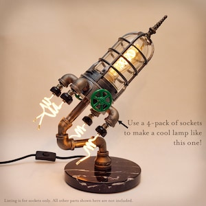 May include: A steampunk-style table lamp made from pipes and a caged light bulb. The lamp has a green valve and a black marble base. "Use a 4-pack of sockets to make a cool lamp like this one!" is written in the image.