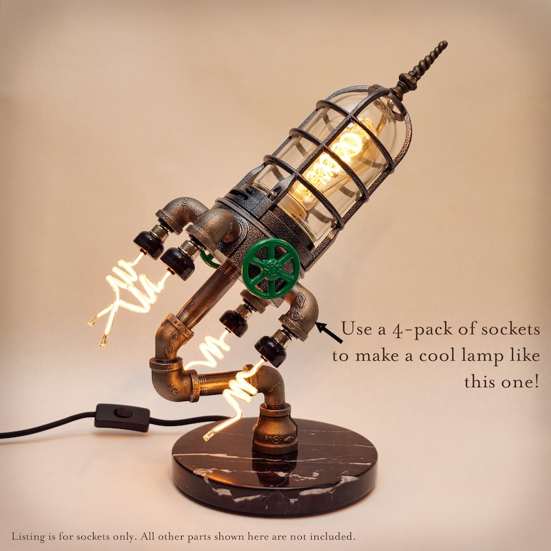 May include: A steampunk-style table lamp made from pipes and a caged light bulb. The lamp has a green valve and a black marble base. "Use a 4-pack of sockets to make a cool lamp like this one!" is written in the image.