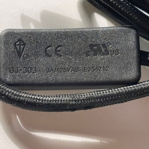 May include: A black rectangular electrical component with a braided cord. The surface features the text OJ-303, 3A/125VAC, E354212, a kite-shaped logo, the CE mark, and the UL recognized component mark for the United States and Canada.