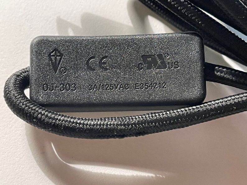 May include: A black rectangular electrical component with a braided cord. The surface features the text OJ-303, 3A/125VAC, E354212, a kite-shaped logo, the CE mark, and the UL recognized component mark for the United States and Canada.