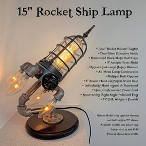 May include: A 38 cm rocket ship lamp featuring a hammered black metal bulb cage, a clear glass protective shade, and four rocket booster lights. The lamp is mounted on a 20 cm round hand-cut poplar wood base with a 7.6 cm antique brass finial.