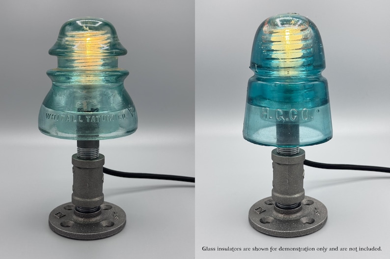 May include: A table lamp featuring a vintage teal glass electrical insulator as a shade, mounted on a dark gray industrial metal pipe base with a circular flange. The lamp includes a warm glowing light bulb and a black power cord.