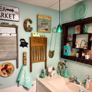 May include: A wall display featuring two vintage washboards, a metal Flea Market sign with an arrow, a letter C, a Fine Fabrics sign, a large safety pin, a wall-mounted shelf with various small items, a clock, and a light blue towel.