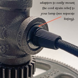 May include: A dark gray metal pipe fitting with a black ribbed cord strain relief and a black fabric-covered electrical cord. The image includes the text: I also offer pipe thread adapters to easily mount the cord strain relief to your lamp.