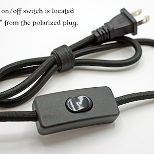 May include: A black fabric-covered electrical cord featuring a polarized plug and an inline on/off switch. The text states: The inline on/off switch is located approx. 30" from the polarized plug. The cord is coiled and secured with a black cable tie.