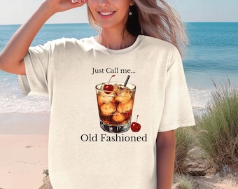 Peut inclure: T-shirt crème avec un graphisme d'un cocktail Old Fashioned, des cerises et de la glace. Le texte "Just Call me... Old Fashioned" est imprimé sous l'illustration du cocktail. Le t-shirt est de coupe ample.