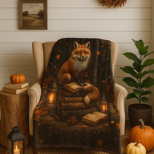 Könnte beinhalten: Gemütliche Szene mit einer Decke mit einem Fuchsmotiv, die über einem Stuhl drapiert ist. Die Decke zeigt einen Fuchs auf Büchern, umgeben von Herbstblättern und Laternen. Der Raum ist mit Kürbissen, einem Kranz und einem "FARMHOUSE"-Schild dekoriert.