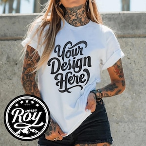 May include: White t-shirt with rolled-up sleeves featuring the text "Your Design Here" in a black, cursive font. A circular logo with the text "verse Roy" and mountain graphic is visible. The model is wearing black shorts.