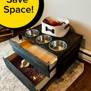 Könnte beinhalten: Eine dunkel gebeizte Holz-Futterstation für Haustiere mit drei Edelstahlnäpfen und zwei Ausziehschubladen. Die obere Schublade enthält einen gewebten Korb mit dem Wort "WOOF" und der Text "Save Space!" befindet sich in einem gelben Kreis.