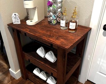 May include: A dark stained wooden coffee bar with a Keurig coffee maker, coffee pods, and glass bottles. White mugs hang from the shelves. The text "Coffee is always a good idea" is on a small sign. The words "BEGINNER FRIENDLY" are at the bottom.