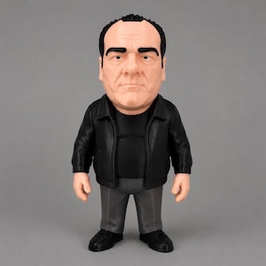 A detailed Tony Soprano collectible figure wearing a black leather jacket, black shirt, grey pants and black shoes. The figure is standing against a clean grey background.