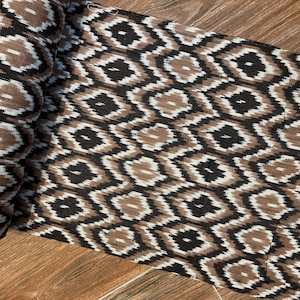 May include: A roll of brown and black ikat fabric with a geometric pattern. The fabric is woven with a white thread, creating a subtle contrast.