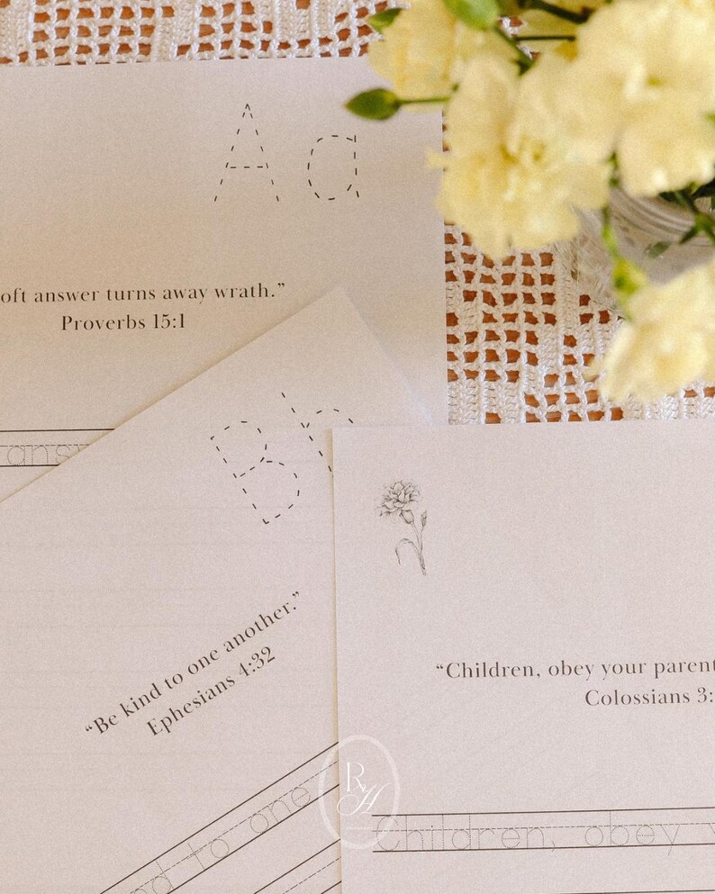 May include: A collection of cream-colored paper sheets with printed text and dotted letters. One sheet features the text "oft answer turns away wrath." Proverbs 15:1. Another sheet reads "Be kind to one another." Ephesians 4:32. A floral arrangement is in the background.