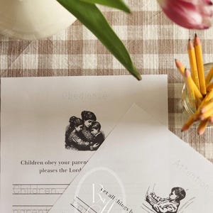 Pu&ograve; includere: Due fogli di carta con testo e illustrazioni, uno con la parola "Obbedienza" e un'immagine di una madre e dei bambini, l'altro con "Attenzione" e un bambino che legge. Matite e un vaso con un tulipano sono sullo sfondo.