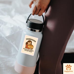 May include: A pale blue water bottle with a black lid and a pink base. The bottle has a sticker that says "Sourdough, the only relationship I've kept alive." The bottle is held by a person wearing maroon leggings.
