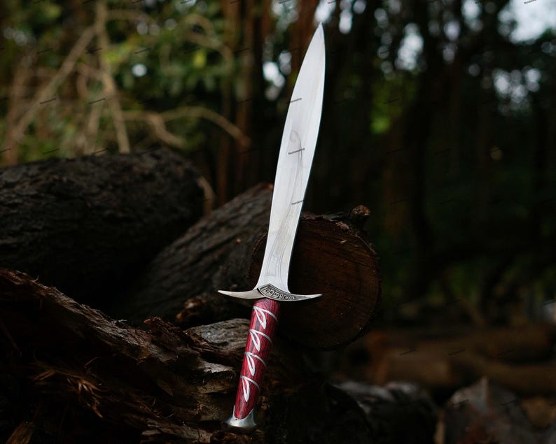 May include: A silver and red dagger with a long, pointed blade. The handle is a deep red with silver accents. The dagger is resting on a weathered log in a forest setting.