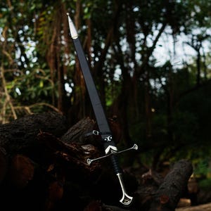 May include: A long, black sword with a silver crossguard and handle, resting against a backdrop of logs and foliage. The sword has a pointed tip and a leather sheath. The overall aesthetic suggests a medieval or fantasy theme.