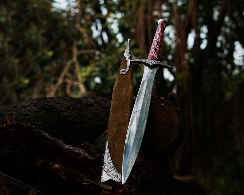 May include: A silver sword with a polished blade and a red and silver handle rests against a brown leather sheath. The sword is displayed on a dark brown log with a blurred forest background.