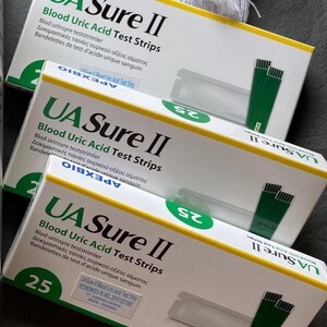 Pode incluir: Tr&ecirc;s caixas de tiras de teste de &aacute;cido &uacute;rico no sangue UA Sure II est&atilde;o empilhadas. As caixas s&atilde;o brancas com detalhes em verde e amarelo. Cada caixa exibe o texto "25" em um c&iacute;rculo verde. As caixas tamb&eacute;m incluem texto em v&aacute;rios idiomas.