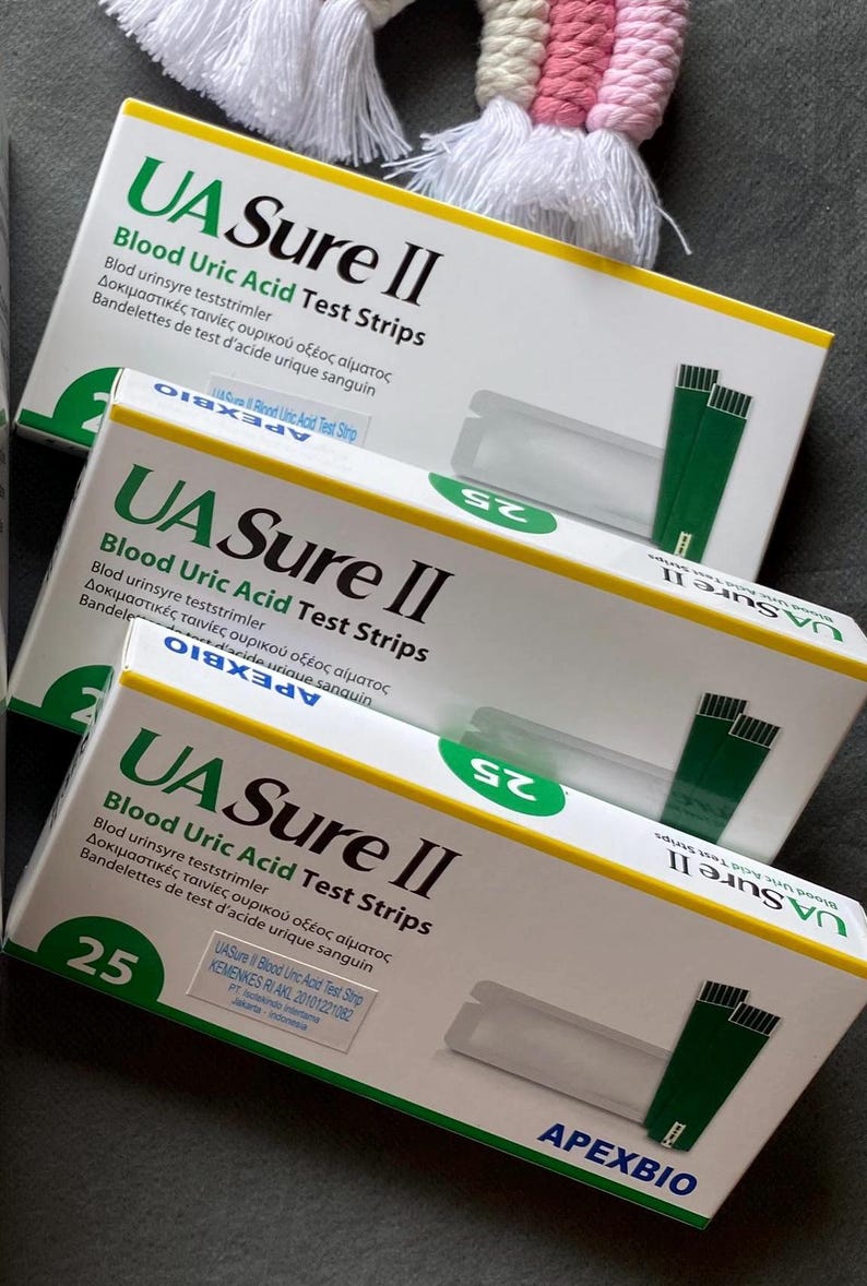 Pode incluir: Tr&ecirc;s caixas de tiras de teste de &aacute;cido &uacute;rico no sangue UA Sure II est&atilde;o empilhadas. As caixas s&atilde;o brancas com detalhes em verde e amarelo. Cada caixa exibe o texto "25" em um c&iacute;rculo verde. As caixas tamb&eacute;m incluem texto em v&aacute;rios idiomas.