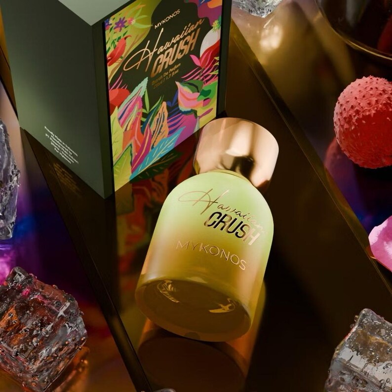 Puede incluir: Un frasco de perfume con tapa dorada y cuerpo degradado amarillo-verde. La botella est&aacute; etiquetada como "Hawaiian Crush Mykonos" en una fuente cursiva. Detr&aacute;s del frasco hay una caja a juego con dise&ntilde;os florales tropicales y el mismo texto. El tema general es la fragancia.