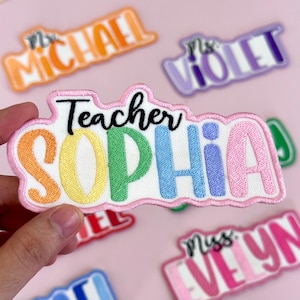 May include: Embroidered patches with names and titles, including "Teacher Sophia," "Ms. Violet," and "Mr. Michael." The patches feature colorful lettering and a white background with a pink border. The patches are designed for teachers.