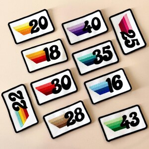 May include: Rectangular white patches with black borders, each displaying a number in bold black font and a colourful, embroidered gradient design. The patches feature numbers like 20, 40, 25, 18, 35, 16, 22, 30, 28, and 43.
