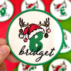 May include: Embroidered Christmas patch with a green number 8, the name "bridget", and a Santa hat with reindeer antlers. The patch has a white background with a green border and festive ornaments.