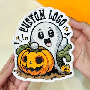 May include: An embroidered patch featuring a white ghost with large black eyes and a smiling mouth, positioned behind a large orange jack-o'-lantern. The text CUSTOM LOGO is arched above the ghost in black letters, with small stars and a bat.