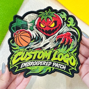 May include: An embroidered patch featuring a red tomato character with a menacing expression holding an orange basketball. The design includes a green basketball hoop, swirling green accents, and the text CUSTOM LOGO EMBROIDERED PATCH.