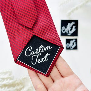 May include: Red and black striped tie with a black label that says "Custom Text" in white script. Two small black squares with the words "Custom Text" are also visible.