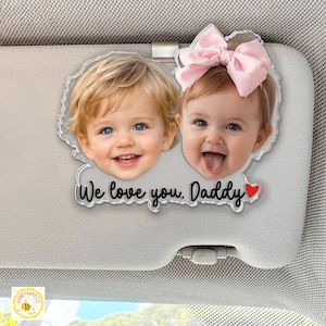 May include: A clear acrylic car visor ornament featuring two smiling children's faces. The text "We love you, Daddy" is below the images, with a red heart. The ornament is attached to a car visor.