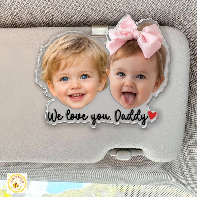 May include: A clear acrylic car visor ornament featuring two smiling children's faces. The text "We love you, Daddy" is below the images, with a red heart. The ornament is attached to a car visor.