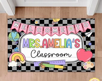 May include: A rectangular classroom doormat with a black and gray checkered background. The mat features the text "WELCOME TO MRS. AMELIA'S Classroom" in colorful letters, along with illustrations of a globe, rainbow, apple, and other school-themed graphics.