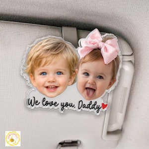 May include: A clear acrylic car visor ornament featuring two smiling children's faces. The ornament has the text "We love you, Daddy" with a red heart. One child has a pink bow.