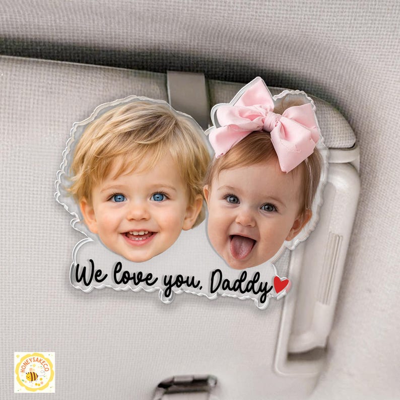May include: A clear acrylic car visor ornament featuring two smiling children's faces. The ornament has the text "We love you, Daddy" with a red heart. One child has a pink bow.