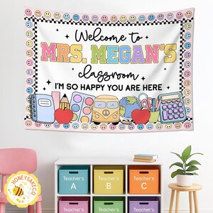 K&ouml;nnte beinhalten: Ein Klassenbanner mit dem Text "Welcome to MRS. MEGAN'S classroom. I'M SO HAPPY YOU ARE HERE." Das Banner hat einen rosa Hintergrund mit Illustrationen zum Thema Schule und einen Rand aus Smileys und Schachbrettmustern.