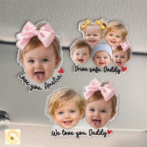 May include: Clear acrylic car charms featuring smiling baby faces with pink bows and the phrases "Love you, Amelia", "Drive safe, Daddy", and "We love you, Daddy". Each charm has a red heart accent.