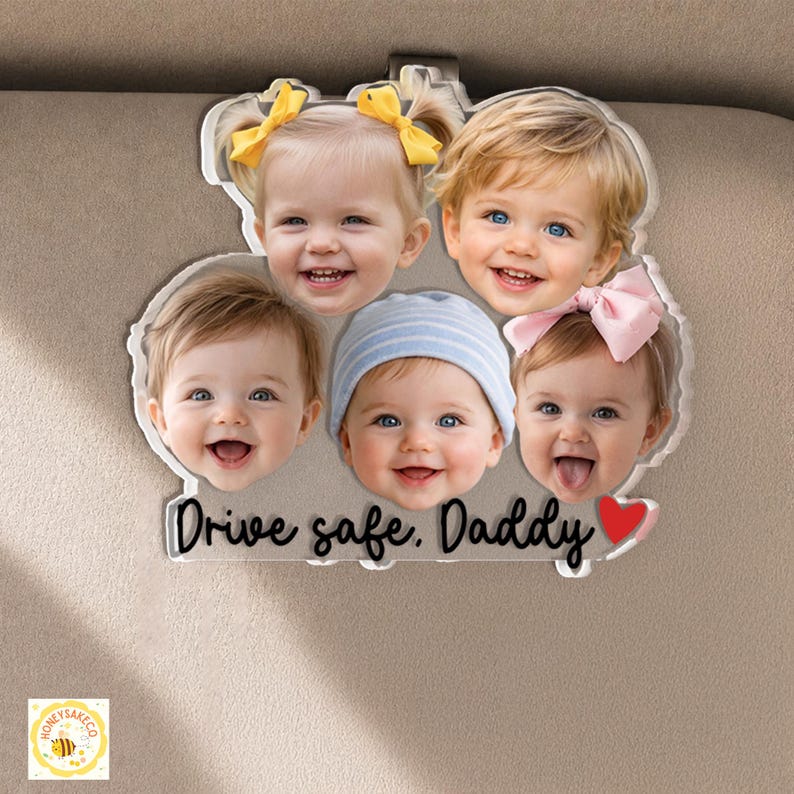 May include: A clear acrylic car visor clip featuring the smiling faces of five babies. The text "Drive safe, Daddy" is written in a cursive font, with a red heart. The clip is designed to attach to a car visor.