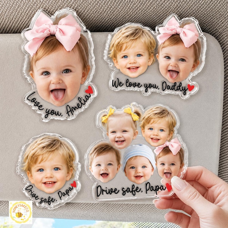 May include: Clear acrylic car visor magnets featuring smiling baby faces. Some magnets have pink bows, and text that reads "Love you, Amelia", "We love you, Daddy", and "Drive safe, Papa".
